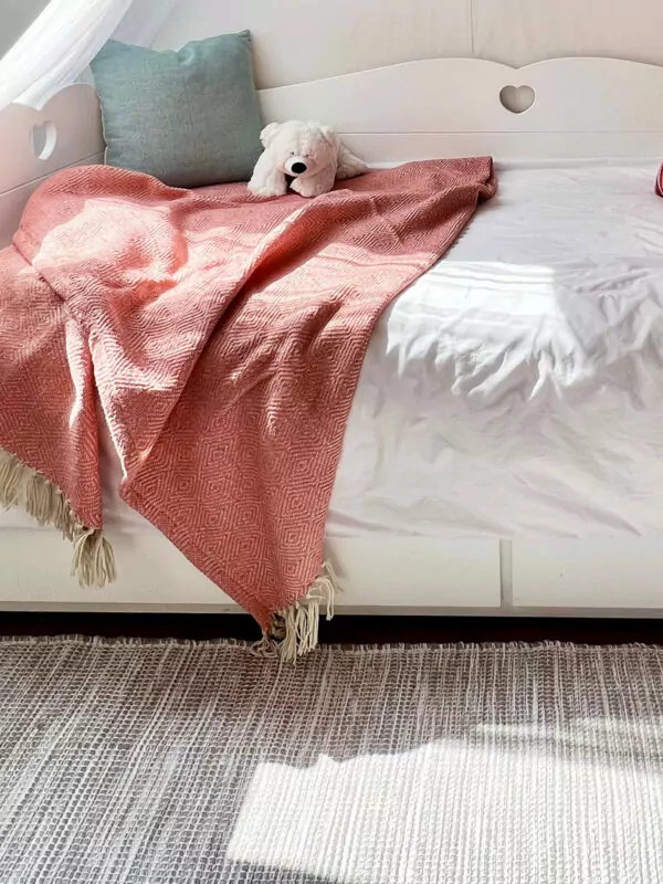 Zandkleurig vloerkleed voor een bed met koraal kleurige deken en aqua groen kussentje