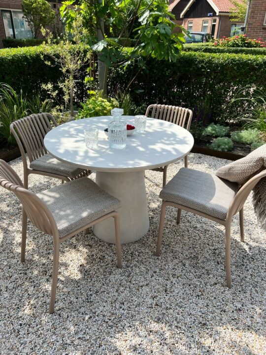 4 stoelen rondom een witte tafel op een kiezelterras met zandkleurige vierkante zitkussens