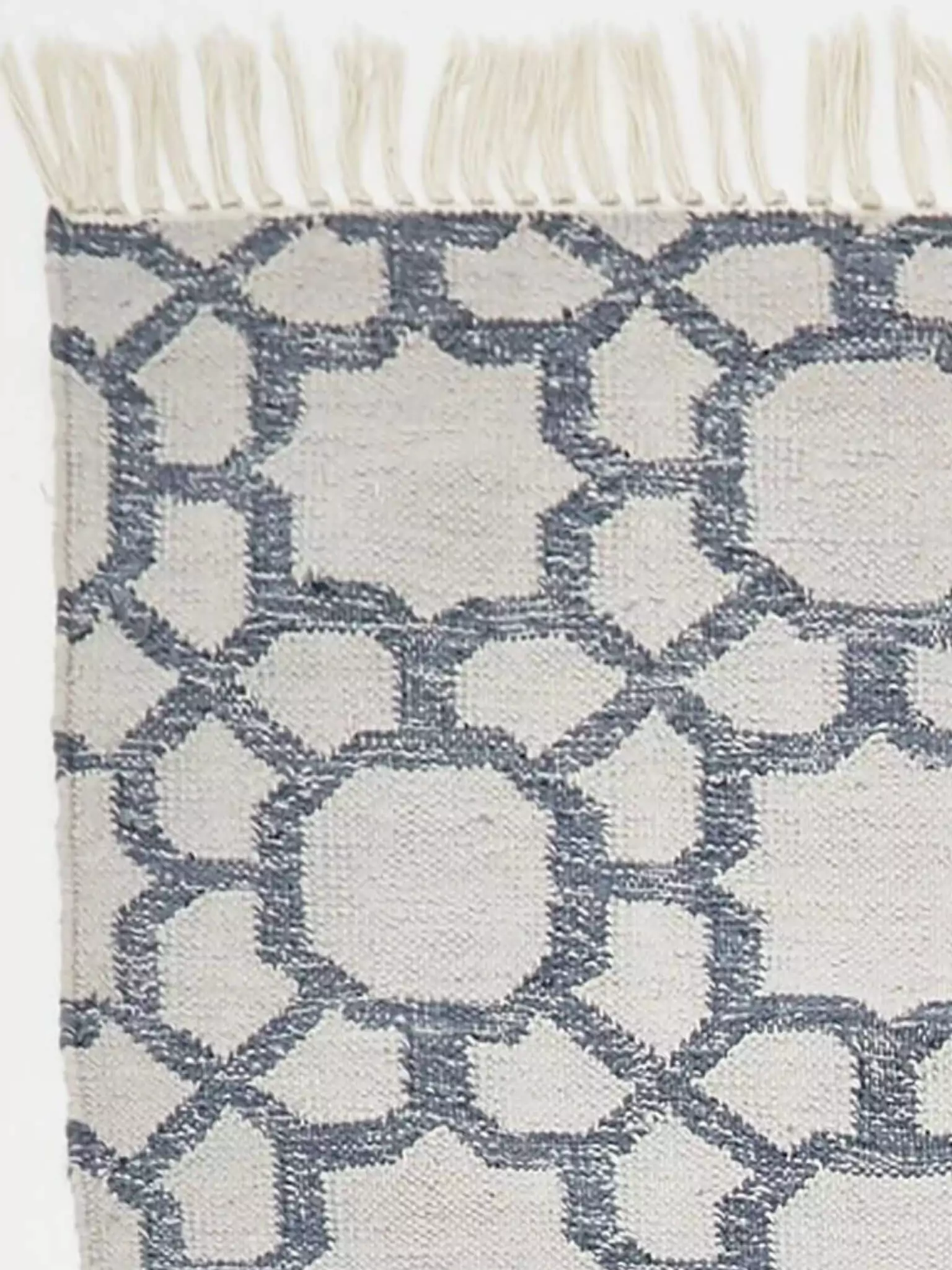 Detailfoto van hoek van vloerkleed grijs met blauw en franjes