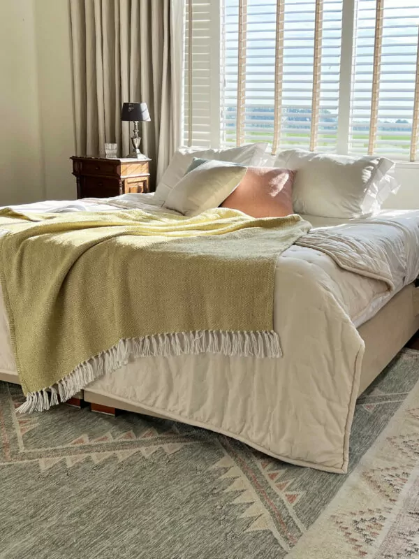 Gele deken gedrapeerd over bed met verschillende kussentjes